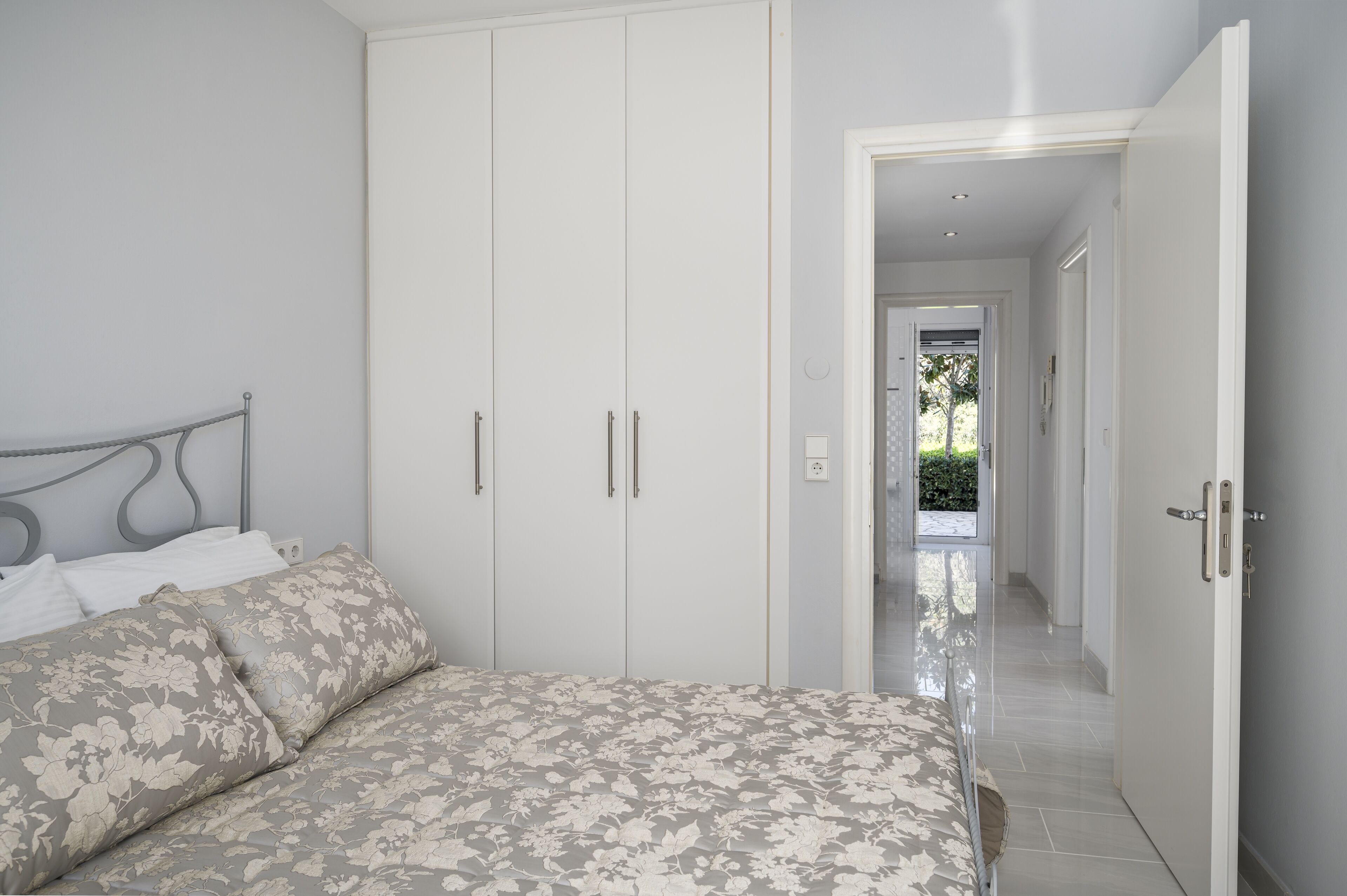 Une chambre à coucher comprenant un lit, une armoire et un couloir menant à un espace extérieur.