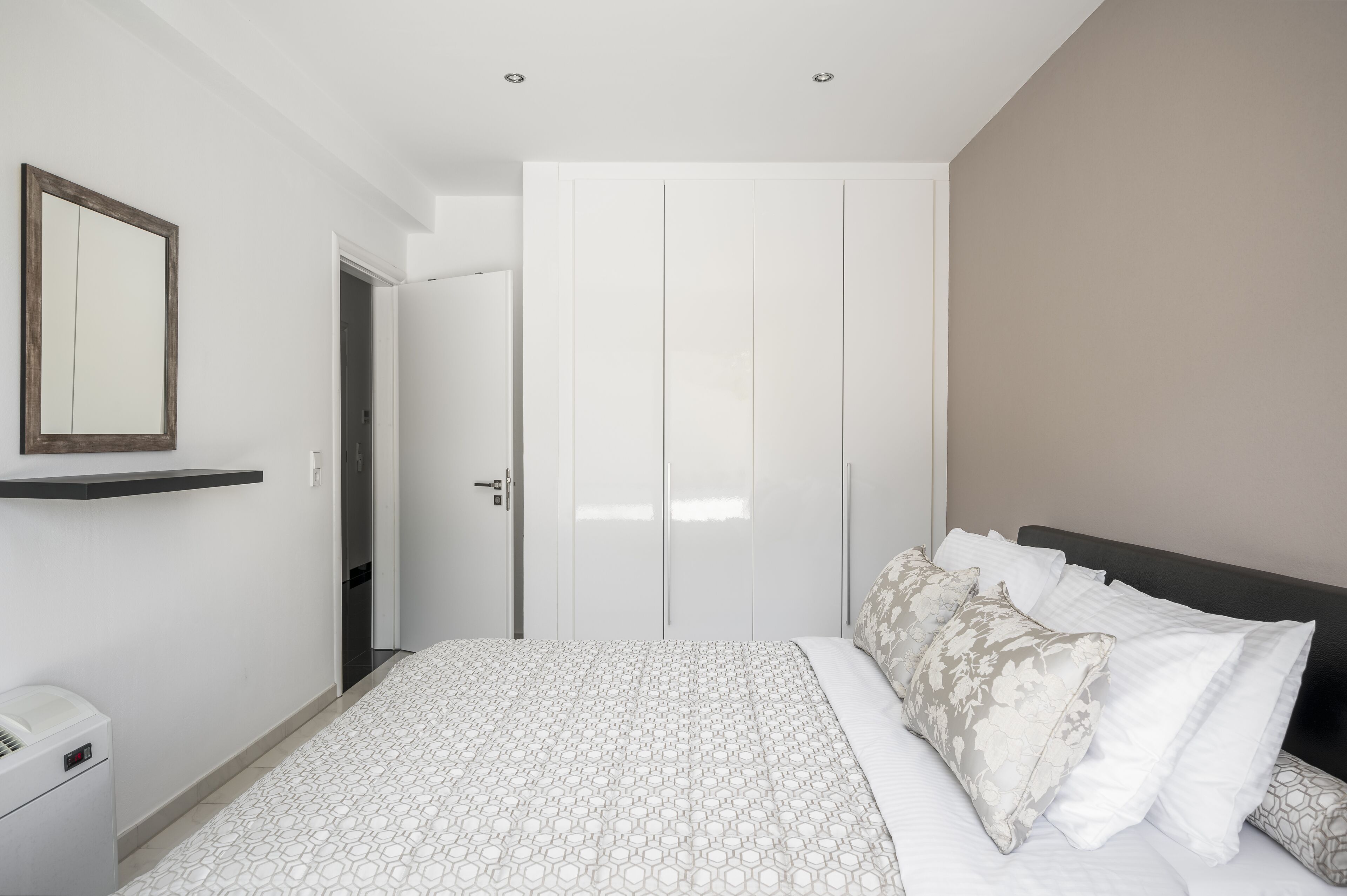 A bedroom with a bed, a wardrobe, a mirror, and a bedside table.
