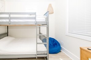 Un lit superposé avec une tête de lit en bois, un fauteuil en forme de poire bleu et une table de chevet avec une lampe.