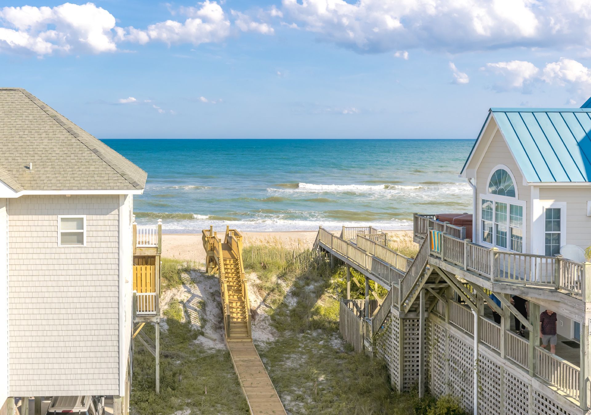 Ein Strandhaus mit einer Holzterrasse, die zum Meer führt, eine kleine Holzhütte und ein Gebäude mit blauem Dach.