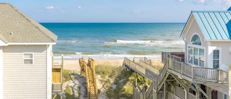 A beach house with a wooden deck leading to the ocean, a small wooden structure, and a building with a blue roof.