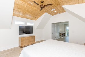 Une chambre avec un plafond en pente, un grand lit, une commode en bois, un téléviseur à écran plat et une vue sur un balcon.