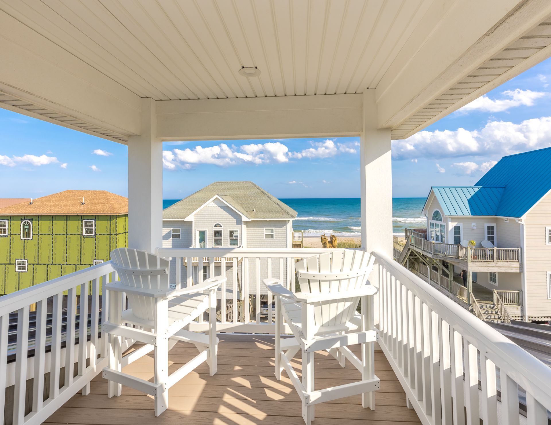 A covered outdoor deck with white railings and two white Adirondack chairs.