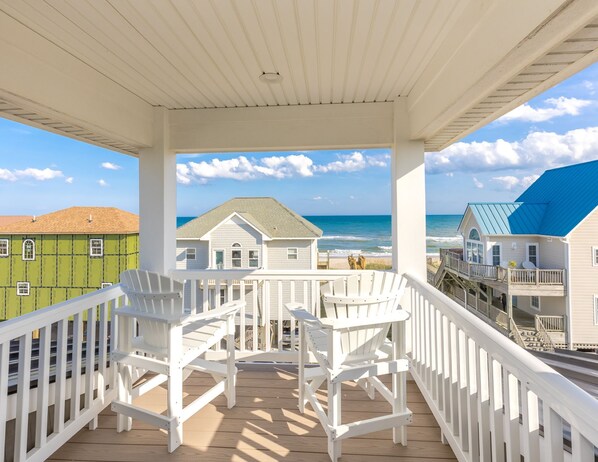 A covered outdoor deck with white railings and two white Adirondack chairs.