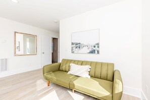 A living room with a green sofa, a white cushion, a framed picture on the wall, and a door leading to another room. - In This Moment - 5 BR Oceanside Home; Elevator; Dog Friendly! (North Topsail Beach)