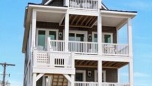 A multi-story building with balconies, a wooden deck, and a clear sky. - In This Moment  - 5 BR New Oceanside Home; Elevator; Dog Friendly! (North Topsail Beach)