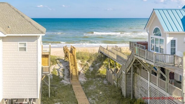 A beach house with a wooden deck leading to the ocean, a small staircase, and a covered porch.