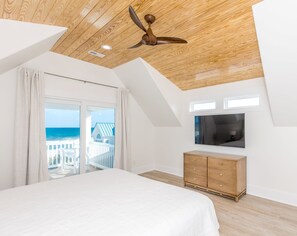 A bedroom with a bed, a wooden ceiling, a TV, and a view of the ocean.