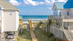 A coastal property with a wooden walkway leading to the beach, a vehicle parked on the left, and a blue-roofed building on the right.