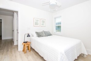 Un dormitorio con cama, escritorio, silla, ventilador de techo y ventana con persianas.