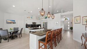 A modern kitchen with white cabinetry, a central island with bar stools, and pendant lighting. - Seagrape Retreat - Walking distance to the beach! (Marco Island)