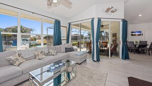 A spacious living room with a large gray sectional sofa, a glass coffee table, and a ceiling fan. - Seagrape Retreat - Walking distance to the beach! (Marco Island)