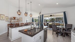 A modern kitchen with a central island, pendant lighting, and a view to the outdoors. - Seagrape Retreat - Walking distance to the beach! (Marco Island)