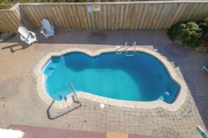 Piscina com deck de madeira, escada de metal e duas cadeiras brancas.