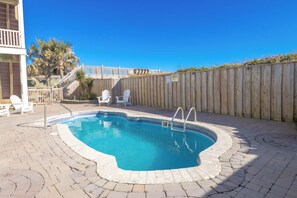 Une piscine avec une terrasse en bois, une clôture en bois et un escalier menant à un balcon.