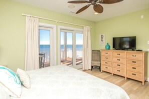 Quarto com cama, cômoda, televisão e vista para o oceano pelas portas deslizantes.