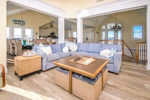 A spacious living room with a large sectional sofa, a coffee table, and wicker ottomans. - Island Life - Amazing Oceanfront 9 BR Home with Pool, Theatre Room & More! (North Topsail Beach)