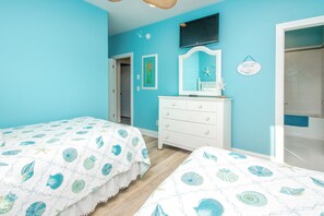 A bedroom with two beds, a dresser, a television, and a bathroom visible through an open door. - Island Life - Amazing Oceanfront 9 BR Home with Pool, Theatre Room & More! (North Topsail Beach)