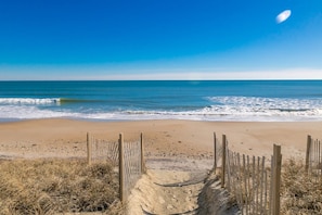 Una playa con valla de madera, orilla arenosa y olas del océano.