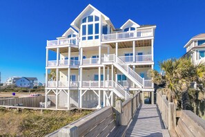 A multi-story beachfront building with balconies, a wooden deck, and a clear sky.