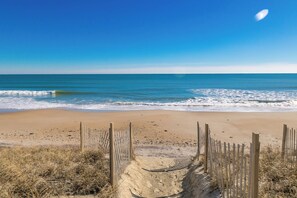 A beach with a wooden fence and dry grass in the foreground.