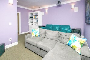 A living room with a grey sectional sofa, teal cushions, and colorful throw pillows. - Island Life - Amazing Oceanfront 9 BR Home with Pool, Theatre Room & More! (North Topsail Beach)