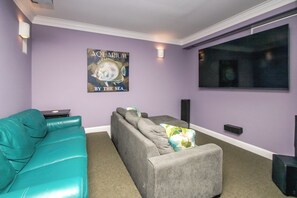 A living room with a teal sofa, a grey sofa, and a poster on the wall. - Island Life - Amazing Oceanfront 9 BR Home with Pool, Theatre Room & More! (North Topsail Beach)