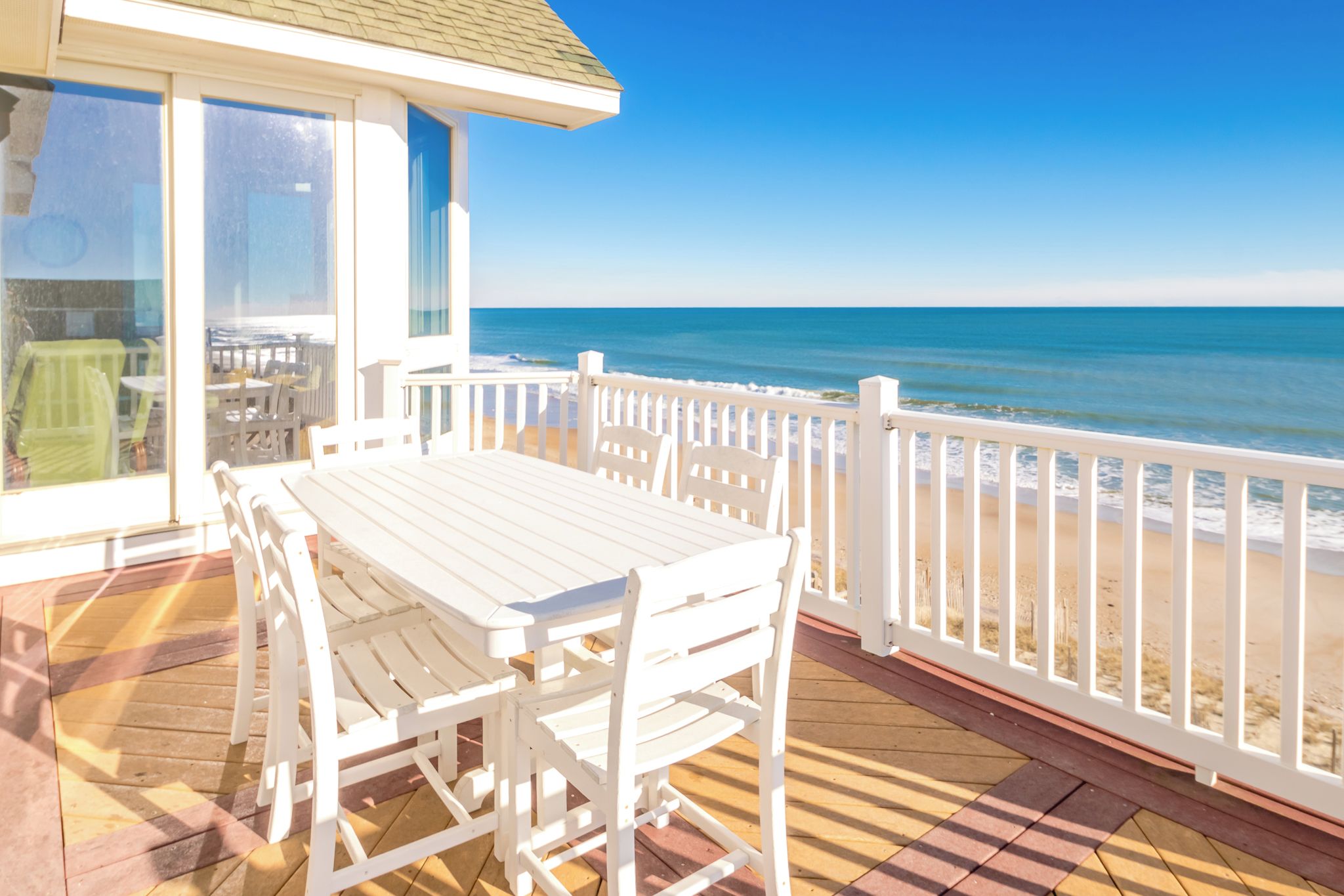 Une terrasse en bois avec une table et des chaises, donnant sur une plage.