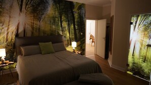 Une chambre à coucher avec un grand lit, une table de chevet avec une lampe et une fresque murale représentant une scène de forêt.