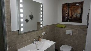 Une salle de bain avec un lavabo blanc, un miroir et un tableau représentant une scène de forêt.