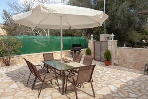 An outdoor patio with a table and chairs, a barbecue grill, and a large umbrella. - Village Loft House (kerkyra)