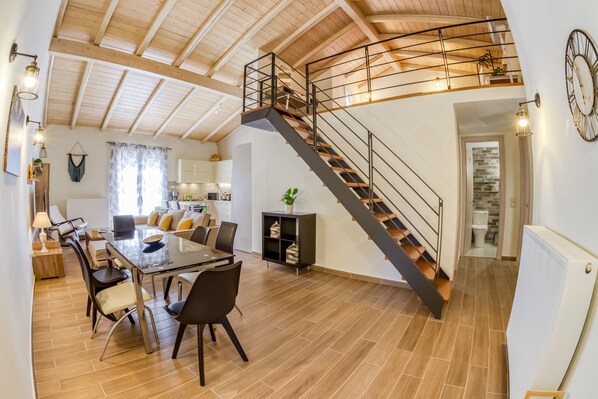 A spacious living area with a dining table, chairs, and a staircase leading to an upper level. - Village Loft House (kerkyra)