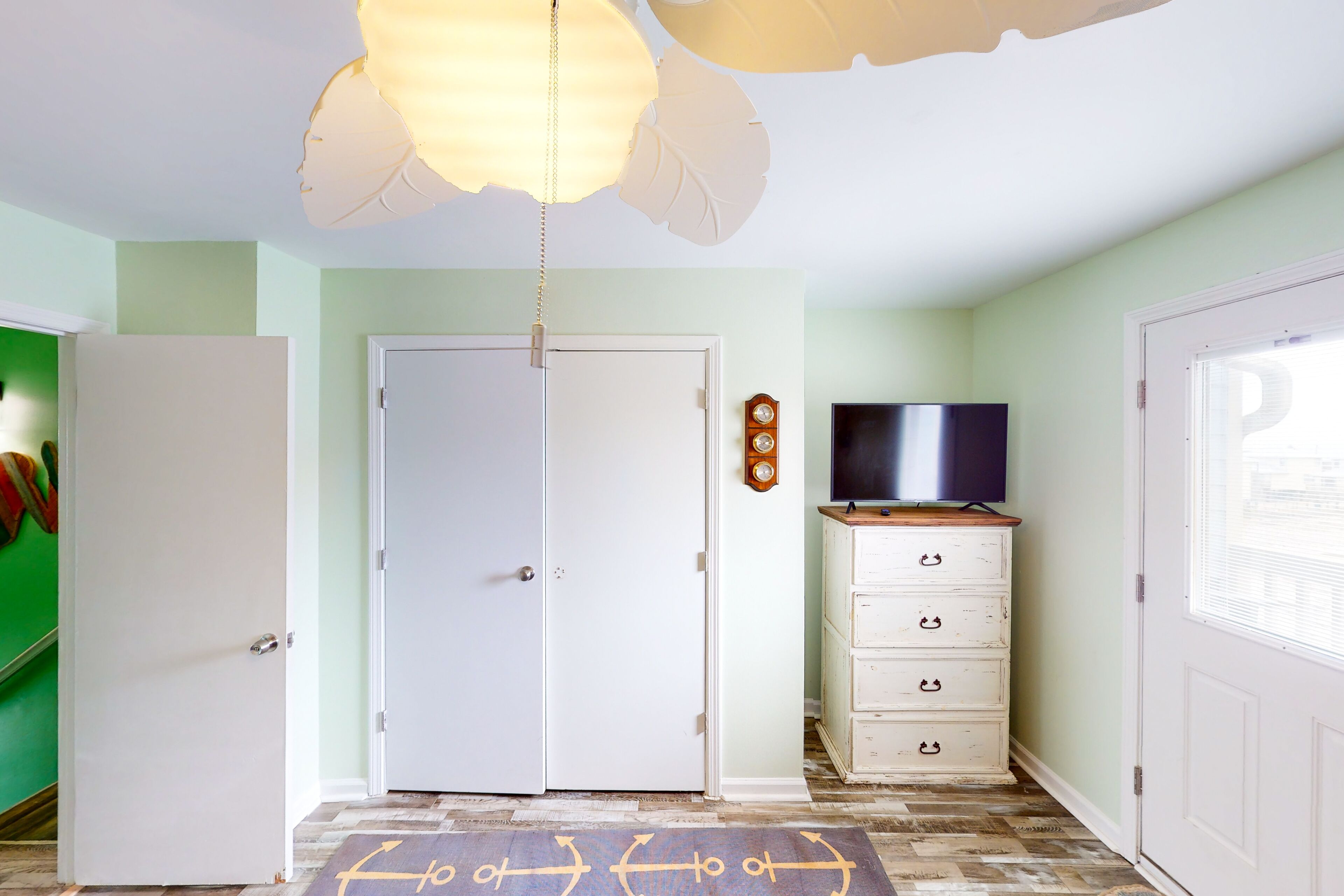 A room with a white door, a television on a wooden cabinet, and a patterned rug on the floor.
