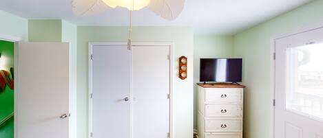 A room with a white door, a television on a wooden cabinet, and a patterned rug on the floor.