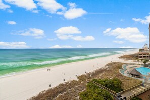 Ein Strand mit blauem Himmel, einem Schwimmbad und einer Promenade.
