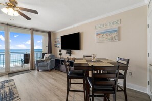 A dining area with a table and chairs, a ceiling fan, and a television mounted on the wall. - FREE Beach Service & Perks! Emerald Beach 732 Pool, Hot Tub, Starbucks, Gym! (Panama City Beach)