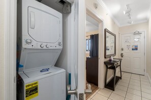 A laundry area with a front-loading washer and dryer, a small table with a sink, and a mirror above the sink. - FREE Beach Service & Perks! Emerald Beach 732 Pool, Hot Tub, Starbucks, Gym! (Panama City Beach)