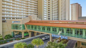 A hotel with a modern design, featuring a prominent glass facade and a red roof. - FREE Beach Service & Perks! Emerald Beach 732 Pool, Hot Tub, Starbucks, Gym! (Panama City Beach)