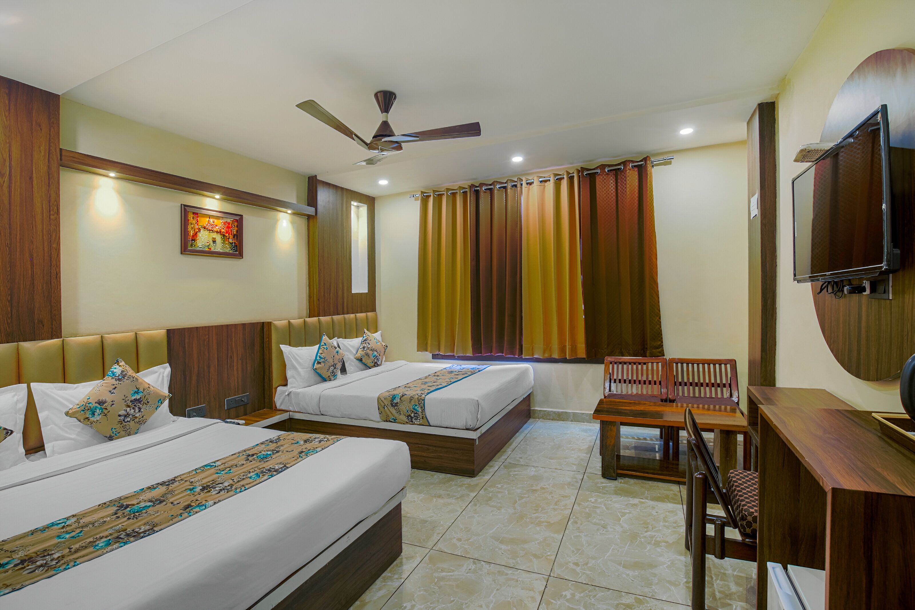 A hotel room with two beds, a desk, a chair, a TV, and a ceiling fan.