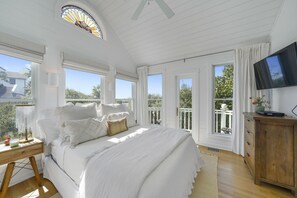 Une chambre avec un grand lit, une table de chevet en bois, une télévision et un balcon avec vue.
