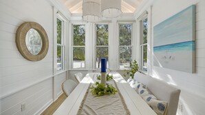 A dining area with a white table, a blue candle, and a painting of a beach. - Lovely Beach Home, Right Across from Beach in Seaside, Fl + 2 Adult Bikes! (Santa Rosa Beach)