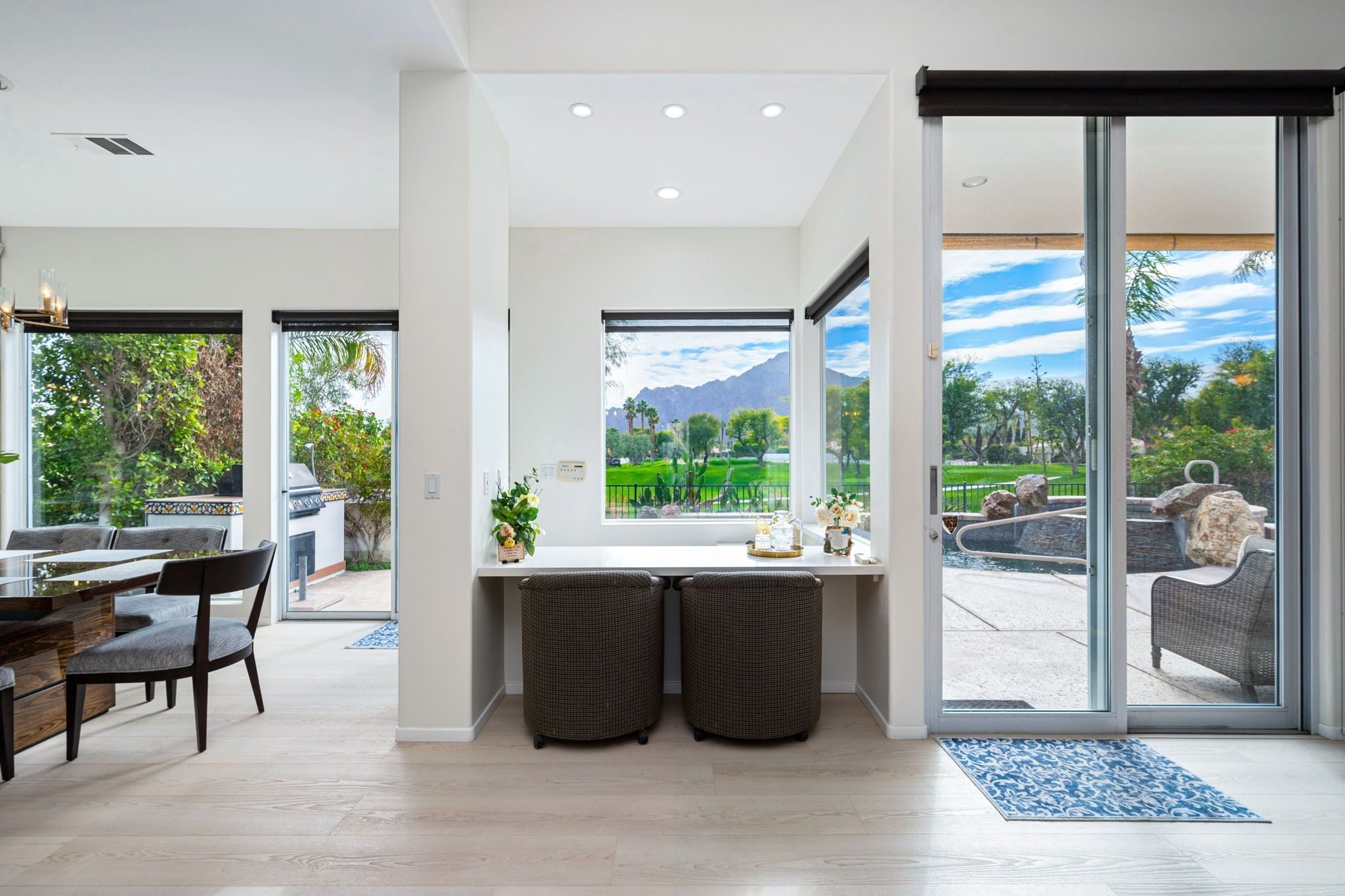 A modern kitchen with a large window, a dining area with a table and chairs, and a view of a landscaped garden.