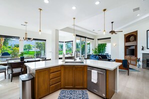 Een moderne keuken met een centraal eiland, grote ramen en een eethoek.