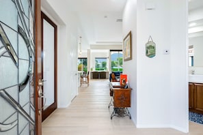 A hallway with a wooden door, a desk, and a view to the outdoors.