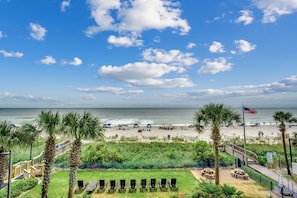 A beach view with a wooden deck, palm trees, and beach chairs.
