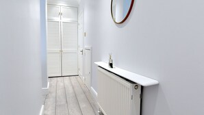 Un pasillo con un radiador blanco, un espejo redondo en la pared y un par de puertas al final.