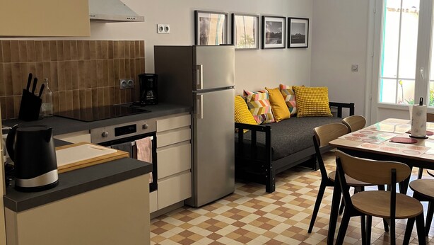 Cocina compacta con refrigerador, estufa y comedor con sillas y mesa.