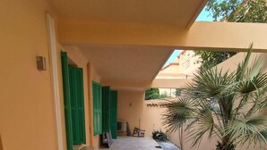 Un espacio exterior cubierto con suelo de baldosas, persianas verdes y plantas en macetas.