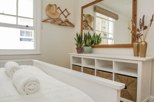 Una cama bien hecha con toallas blancas enrolladas, una consola blanca con plantas en macetas, un espejo y una ventana con vistas al exterior.