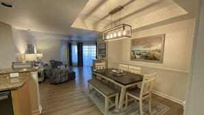 Una cucina moderna con piani in granito, una zona pranzo con tavolo e sedie in legno e un soggiorno con divano decorato e ventilatore a soffitto.